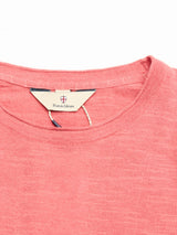 A close-up of the BGmonty Knit - Coral T-shirt by Blue de Gênes, highlighting its red heathered cotton-linen blend, neckline, and beige interior tag featuring a small logo and the Blue de Gênes name.
