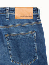 Close-up of the back of BGrepi Kanto Jeans - Used by Blue de Gênes in blue slim-fit comfort stretch denim, featuring a brown leather patch above the pocket with Blue de Gênes branding and a small shield logo on the right.