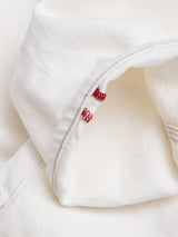 A close-up of the premium white fabric on Blue de Gênes BGvinci Bianco Jeans, showcasing a folded edge with beige stitching and red zigzag embroidery—distinctive details of these Italian-crafted regular fit jeans.