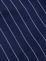 Close-up of the BGpalco Toll Pants - Navy Stripe by Blue de Gênes, showcasing dark blue fabric with evenly spaced, thin white vertical pinstripes running diagonally from top left to bottom right. The slightly visible texture emphasizes the quality craftsmanship typical of premium striped cotton pants.