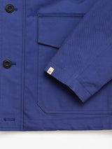 A close-up of the BGcanopy Jacket - Navy Peony by Blue de Gênes shows black buttons, a large front pocket with a flap, and a small white tag with a red and blue logo on the sleeve. The sturdy, well-stitched fabric highlights the jacket’s classic workwear heritage.