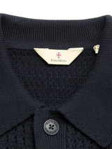 Close-up of the BGbilly S/S Cardigan in dark navy, highlighting its knit collar with a button and a Blue de Gênes label adorned with a small shield emblem above the brand name. Crafted from 100% cotton, this vintage-inspired piece seamlessly blends comfort and timeless style.