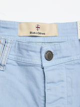 Close-up of Blue de Gênes BGpaulo Pavia Pant in Blue Fog, crafted from cotton stretch fabric with a shield-engraved button and a Blue de Gênes label above the waistband beneath a red and white shield design.