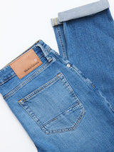 The BGvinci Hera Used Jeans by Blue de Gênes feature a mid blue wash, brown leather branded patch, and a cuffed leg that reveals the inner fabric. Made from comfort stretch denim for easy, everyday wear.