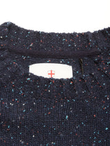 Close-up of the Honshu Crewneck Knit - Navy by Blue de Gênes, showing its ribbed neckline and colorful speckled lambswool fabric. The chunky knit sweater features a white inner tag with a red cross emblem.