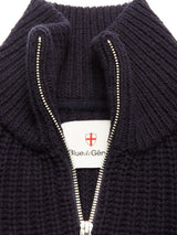 Close-up of the Blue de Gênes Yomaha Halfzip Knit in navy, a ribbed wool blend sweater featuring a partially open silver half-zip detail that reveals a white label with a red shield logo and the brand name inside the collar.