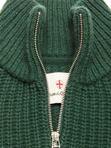 Close-up of the Blue de Gênes Yomaha Halfzip Knit in Scarab, featuring a green ribbed texture and a partially open silver zipper that reveals a white tag with a red shield logo and black text.