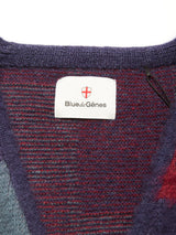 Close-up of the Block Knit Cardigan - Navy Pattern by Blue de Gênes, featuring a neckline with the brand’s label and red and white shield logo on a textured, multi-color block knit fabric in shades of red, purple, and blue.
