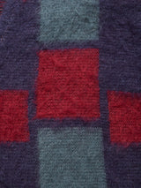 A close-up of the Block Knit Cardigan - Navy Pattern by Blue de Gênes, showcasing its textured fabric with a geometric pattern of red and teal squares on a dark purple background, reminiscent of a multi-color block knit wool blend.