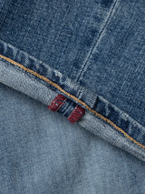 Close-up of BGvinci Girisha Used Jeans by Blue de Gênes, featuring blue denim fabric with a folded hem, orange stitching, and a red and white selvedge edge.