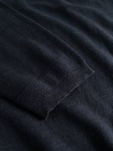 A close-up of the BGmonty Knit - Dark Navy by Blue de Gênes displays a folded sleeve with ribbed cuff detailing and a roll-rib hem, laid flat on a matching dark navy fabric background.