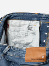 A close-up of BGvinci Pala Used V2 Jeans by Blue de Gênes, regular fit denim blue, waistband folded to reveal a leather brand patch and printed inner label. Made from comfort stretch denim for ease.
