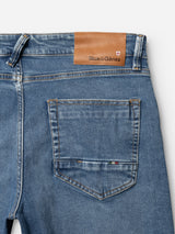 Close-up of the back of BGvinci Pala Used V2 Jeans in denim blue by Blue de Gênes, made in Italy from comfort stretch denim. Features a brown leather brand patch and a small flag detail above the right back pocket.