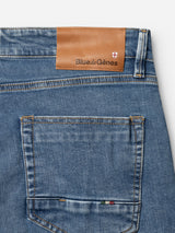 Close-up of the back pocket of BGvinci Pala Used V2 Jeans in denim blue by Blue de Gênes, featuring a brown leather patch with the brand name and shield logo above it, and brown thread stitching.