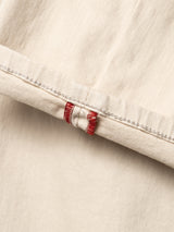 Close-up of BGpaulo Pavia 1 V2 Chino - Ecru by Blue de Gênes, showing folded beige cotton stretch denim edge, visible white stitching, and a small red and white tab detail inspired by vintage military pants.