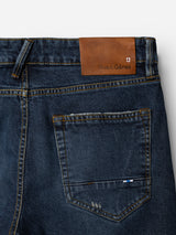 Close-up of the BGvinci Arrow Jeans - Denim Blue by Blue de Gênes, highlighting the dark blue denim back pocket and waistband with a brown leather "Blue de Gênes" patch and a small stitched flag detail near the pocket. Crafted from comfort stretch denim, these regular fit jeans deliver both flexibility and contemporary style.