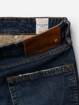 Close-up of blue denim jeans featuring a brown leather patch embossed with Blue de Gênes and an interior fabric label reading "Candiani Denim Italian Premium Dream Fabric." The BGvinci Arrow Jeans – Denim Blue offer a regular fit crafted from comfort stretch denim, blending style and ease, inspired by the craftsmanship of Vinci Jeans.