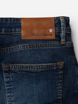 Close-up of the BGvinci Hermina Jeans - Med Used by Blue de Gênes, crafted from comfort stretch dark blue denim. A brown leather patch above the back pocket displays the Blue de Gênes name and a small white cross emblem, underscoring the signature style of these regular fit jeans.