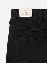 Close-up of the BGrepi TrueBlack Jeans by Blue de Gênes, featuring black slim-fit denim crafted from comfort stretch fabric with visible stitching details. A cream-colored Blue de Gênes brand tag, adorned with the signature red and white shield logo, is partially tucked into the waistband.
