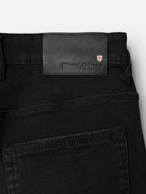 Close-up of the back pocket and waistband of the Blue de Gênes BGrepi TrueBlack Jeans, crafted from comfort stretch black denim for lasting wear, featuring a black leather patch embossed with “Blue de Gênes” next to a small shield emblem with a red cross.