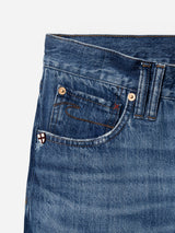 Close-up of the upper section of blue cotton denim BGmarco Sioux Jeans - Used by Blue de Gênes, featuring the waistband, belt loops, a small pocket with a red stitch, copper rivets, and a small white patch with a red cross. This classic design showcases the signature relaxed fit jeans style from Blue de Gênes.