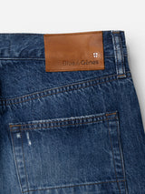 Close-up of the back pocket and waistband of the blue BGmarco Sioux Jeans - Used by Blue de Gênes, featuring a brown leather patch embossed with the Blue de Gênes name and shield logo. These cotton denim jeans display prominent stitching, subtle fading, and offer a relaxed fit for everyday comfort.