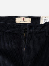Close-up of the BGpalco Cord Chino in Navy by Blue de Gênes, featuring a dark blue relaxed fit with tapered legs. Details include a visible brass zipper, black button, and a Blue de Gênes label adorned with a small crest. A care tag is partially visible on the right, highlighting the brand’s commitment to quality craftsmanship and attention to detail.
