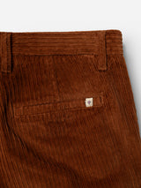 Close-up of the BGpalco Cord Chino in Ginger Bread Orange by Blue de Gênes, highlighting the relaxed fit waistband, belt loop, back pocket, and a small stitched shield logo patch above the pocket. The tapered silhouette brings a contemporary feel to this classic corduroy design.