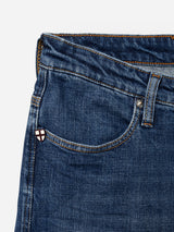 Close-up of the BGrepi Callum Jeans - Mid Blue Denim from Blue de Gênes, highlighting the classic five-pocket design in blue denim. The front pocket, belt loop, and a small pin featuring a red and white cross shield near the pocket seam are clearly visible. Distinctive stitching and the comfortable stretch denim texture are showcased in detail.