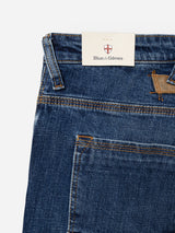 Close-up of the BGrepi Callum Jeans in mid blue denim by Blue de Gênes, showcasing the pocket with brown stitching and a branded tag tucked under the waistband featuring a shield logo with a red cross. Crafted from comfort stretch denim, these jeans offer both durability and ease of movement.
