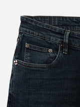 Close-up of the top front section of the BGvinci Ewan Jeans - Color Denim by Blue de Gênes, featuring a regular fit in a dark blue wash with visible waistband, belt loop, pockets, and a small patch with a red cross on a white background near the coin pocket. Crafted from comfort stretch denim for easy wear throughout the day.