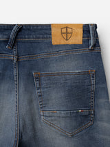 Close-up of the back pocket of Blue de Gênes BGvinci OM Jeans - Denim wash, featuring orange stitching, a small Italian flag tag on the pocket, and a tan leather patch with a shield logo on the waistband. The authentic worn-in denim wash enhances these regular fit jeans, showcasing their timeless style and quality craftsmanship.