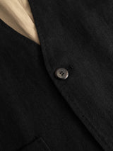Close-up of the BGduncan Ian Gilet in Black by Blue de Gênes, featuring a single black button fastened at the front and revealing part of a beige inner lining or shirt beneath. The sharp lapel edge and pocket are visible, highlighting the refined layering potential of this piece—perfect for combining with a linen waistcoat or three-piece suit in lightweight textured fabrics.