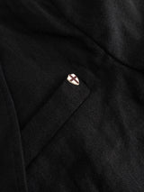A close-up of the BGleopardi Ian Blazer in black by Blue de Gênes, featuring a small lapel pin with a white shield and red cross attached above the pocket.