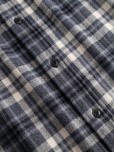 Close-up of the BGenrico Hang Shirt - Navy Check by Blue de Gênes, featuring a blue, white, and gray plaid check pattern with black buttons. The woven texture of the 100% cotton fabric and classic collar are clearly visible, along with detailed button accents.