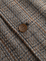 Close-up of a brown button on the textured, grey check herringbone-patterned fabric of the BGmungo Check Overshirt by Blue de Gênes—a men’s regular fit wool-blend overshirt.