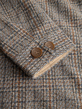 Close-up of the sleeve of the Blue de Gênes BGmungo Check Overshirt in Grey Check, showcasing a herringbone-patterned tweed fabric in blue, beige, and orange tones with two brown buttons—highlighting the intricate weave and classic overshirt style.
