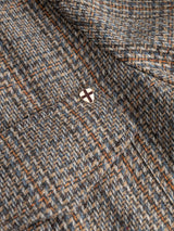 Close-up of the BGmungo Check Overshirt by Blue de Gênes, showcasing its grey check tweed fabric with a classic herringbone pattern. A small metallic pin featuring a black cross on a white background is attached near the seam.