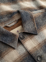 Close-up of the Blue de Gênes BGyodo Check Overshirt in Grey Check, showcasing its brown and beige striped wool fabric with a soft, textured appearance. Details include dark buttons and a visible inside label featuring a red cross emblem and partial text, highlighting the men’s regular fit design.