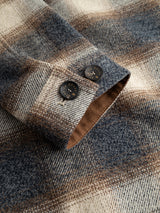 A close-up of the BGyodo Check Overshirt - Grey Check by Blue de Gênes showcases the plaid wool sleeve in blue, brown, and cream tones, featuring two dark engraved buttons against a light background.