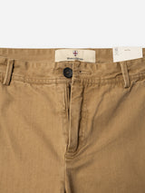 Close-up of the BGmenzo Rory Chino in khaki by Blue de Gênes, featuring tan washed herringbone fabric with a black button, belt loops, partial zipper, and a branded label on the inner waistband. A partially visible white tag at the waist highlights its classic chino fit—ideal for pairing with a matching blazer.