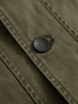 Close-up of the BGgabbiano Rory Blazer - Army by Blue de Gênes, featuring olive green washed herringbone fabric, a metal button with engraved text, and visible seam stitching.