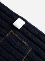 A close-up of the BGcomforto Knit Scarf in Dark Navy by Blue de Gênes, showcasing its dark blue ribbed knit texture, a sewn-on tag reading 100% ACRYLIC, and a brown-stitched rectangular patch.