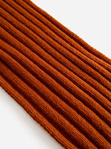 Close-up of the BGcomforto Knit Scarf in Ginger Bread Orange by Blue de Gênes—a ribbed, knitted fabric showcased diagonally against a white background, evoking the look of a cozy, chunky knit.