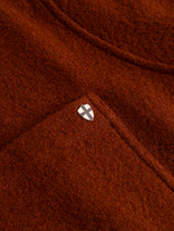 A close-up of the Blue de Gênes BGhew Wool Overshirt in Ginger Bread Orange, highlighting its textured boiled wool fabric, stitched pocket, and a small shield-shaped pin with a white cross on a black background.