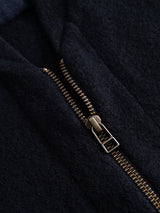 A close-up of a partially unzipped brass zipper on the dark navy fabric of the BGmudock Wool Waistcoat by Blue de Gênes, highlighting the textured material and zipper teeth.
