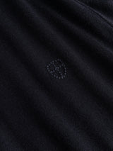 A close-up of dark navy merino wool fabric from the Blue de Gênes BGhamish Crewneck Knit, featuring a subtle embroidered shield-shaped logo in the center.