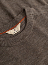 A close-up of a sepia tint brown BGhamish Crewneck Knit by Blue de Gênes showcases its ribbed collar. The lightweight merino wool sweater features a visible Blue de Gênes tag with a small crest and includes a thin orange accent stripe along the inside neckline.