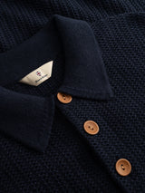 Close-up of the BGmurry Polo Knit in Dark Navy from Blue de Gênes, featuring a textured knit design with a collar and three brown buttons. This stylish piece embodies the refined aesthetic of a knitted polo, with a small white label—bearing the Blue de Gênes logo and text—visible inside the collar.
