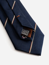 A close-up of the BGshield Tie - Dark Navy by Blue de Gênes, featuring folded diagonal stripes in white, red, and olive. The tie’s inner label and stitching details are visible against a plain white background.